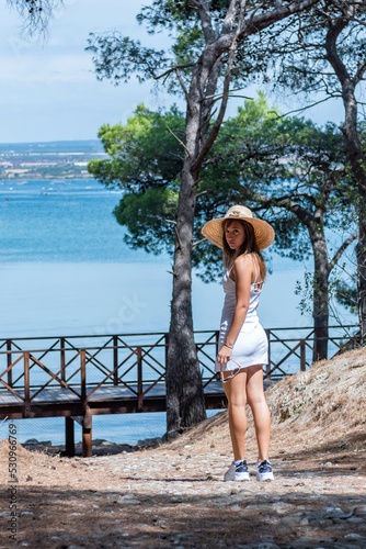 Beautiful Girl Walking under Trees in frot of the Ionian Sea in Summer dressing Hay Hat. Concept of Happiness and Freedom photo