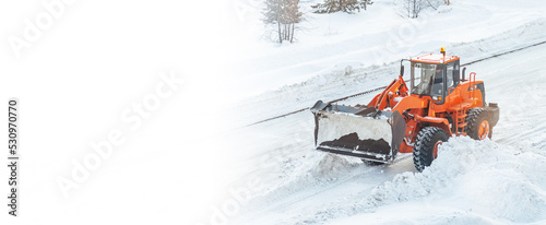 A large orange tractor removes snow from the road and clears the sidewalk. Cleaning and clearing roads in the city from snow in winter. Snow removal after snowfalls and blizzards. banner