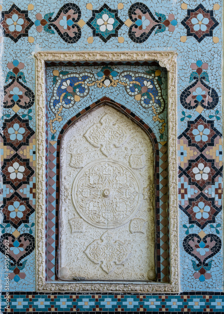 Closeup of beautiful traditional geometric and floral design in white stucco with blue mosaic frame on the exterior wall of ancient Sar-i-Mazor mausoleum, Istaravshan, Sughd region, Tajikistan