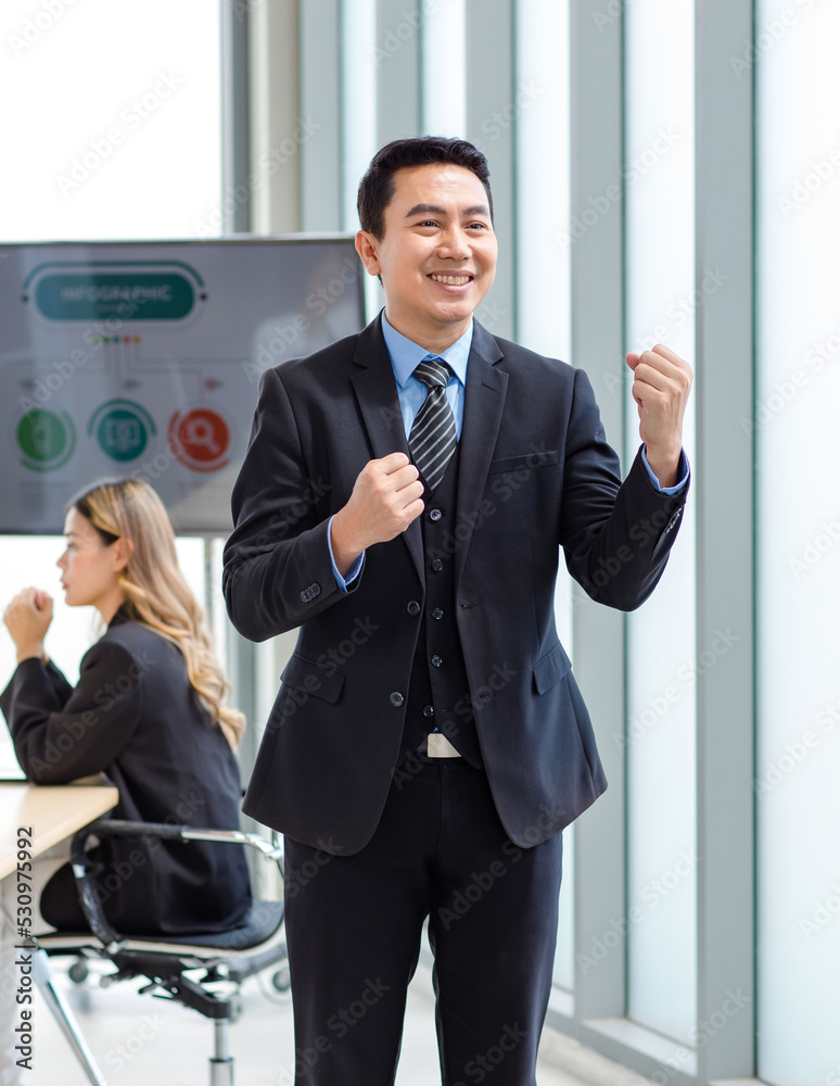 Millennial Asian happy successful professional male businessman entrepreneur in formal suit standing smiling in company office meeting room with big screen monitor Millennial Asian happy successful professional male businessman entrepreneur in formal suit standing smiling in company office meeting room with big screen monitor