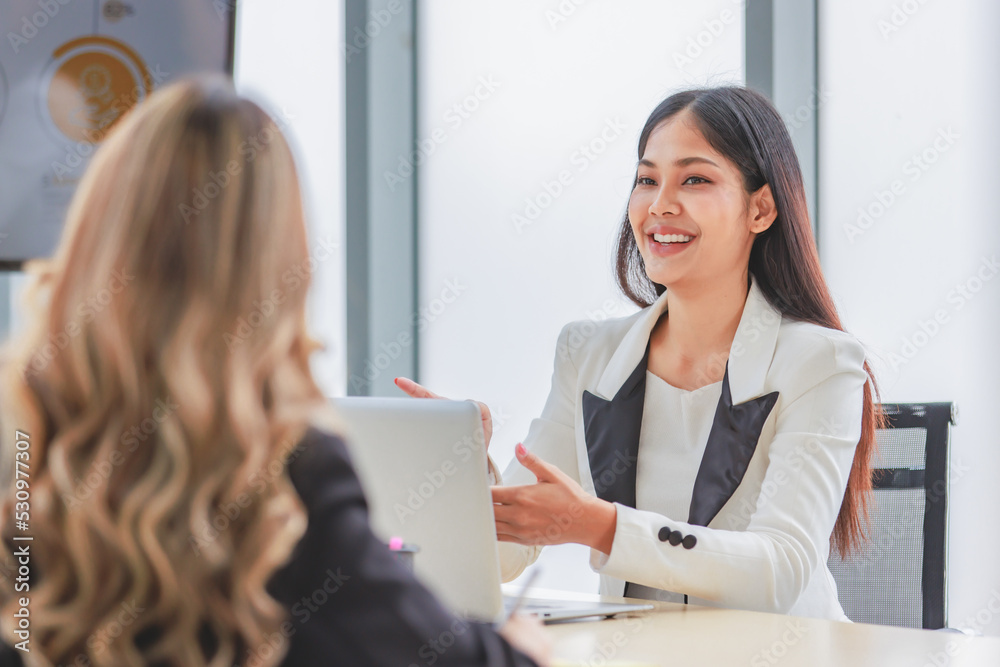 Closeup shot of Millennial Asian beautiful successful professional female businesswoman employee in formal suit sitting smiling talking to colleagues at working desk in company office meeting room Closeup shot of Millennial Asian beautiful successful professional female businesswoman employee in formal suit sitting smiling talking to colleagues at working desk in company office meeting room