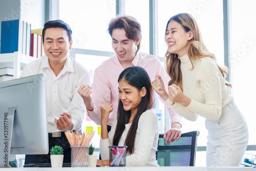 Millennial Asian beautiful successful professional businesswoman sitting smiling pointing finger showing data information on computer monitor to male businessmen female colleague in company office