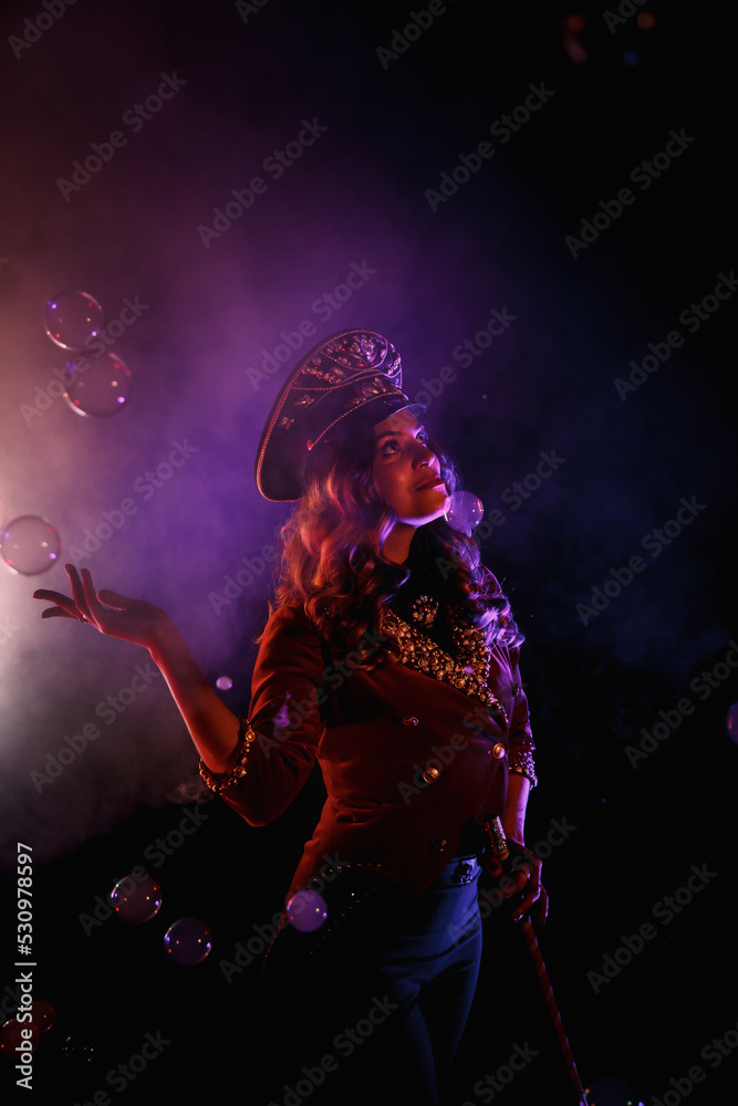 Female magician illusionist circus with stylish hat in shows soap bubbles show at black background. Woman actress theatrical clothes in stage costume. Concept of theatre performance. Copy space