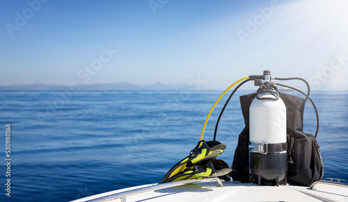 A scuba diving tank and gear standing on a boat bow with blue sea and sunshine as a banner with copy space photo