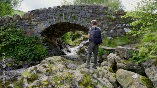 Boy standing at Ashness Bridge is an old packhorse bridge with wonderful views looking back towards the lake.it is probably the most photographed,and very popular with visitors. photo