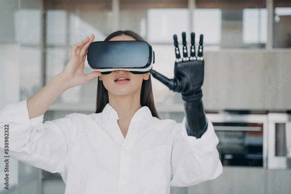 Girl with bionic prosthetic arm wearing virtual reality glasses touch objects in VR by robotic hand Girl with bionic prosthetic arm wearing virtual reality glasses touch objects in VR by robotic hand
