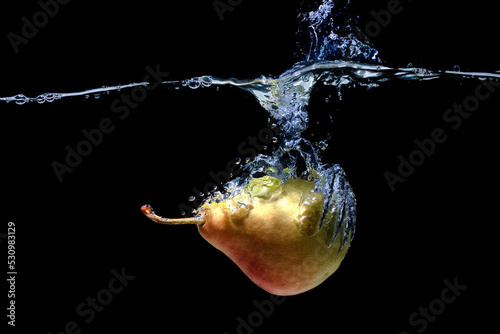 Fresh pear dropped in water with splashes on black