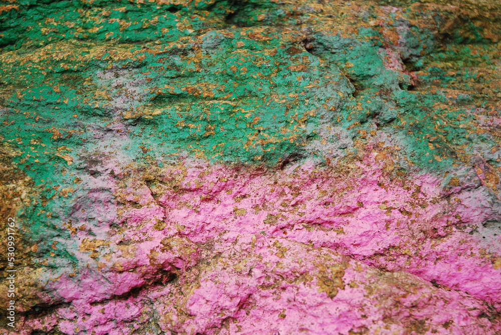 Brown stone painted with paint in pink and green. Rock background, texture. Pattern.