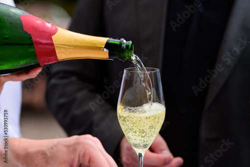 closeup of a champagne bottle pooring champagne into a champagne flute against a blurred person at a party