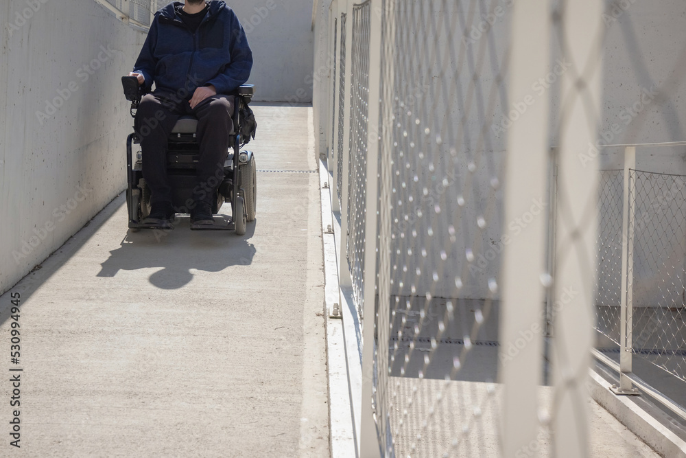 Man on wheelchair, approaching the building moving along an accessible ramp for persons with disability