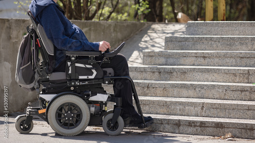 Person with disability on electric wheelchair stopping at the bottom of inaccessible staircase, unable to reach the top photo