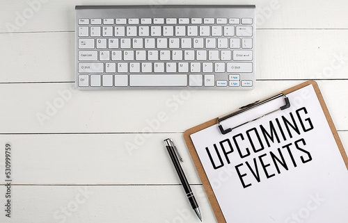 Home office workspace with keyboard, clipboard and pen with text UPCOMING EVENTS on white wooden background , business concept