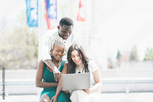 gruppo di giovane ragazze multietniche amichevoli con laptop che leggono informazioni online mentre si preparano per il seminario all'aperto photo