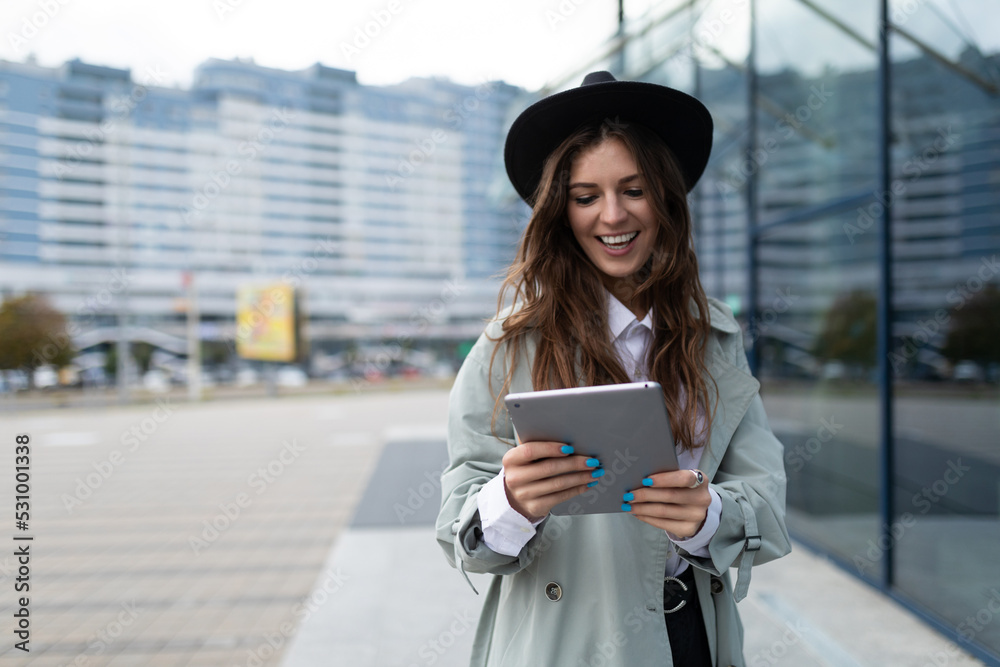 Fototapeta premium young stylish woman looking at a tablet against the backdrop of a glass facade of an office building in the city