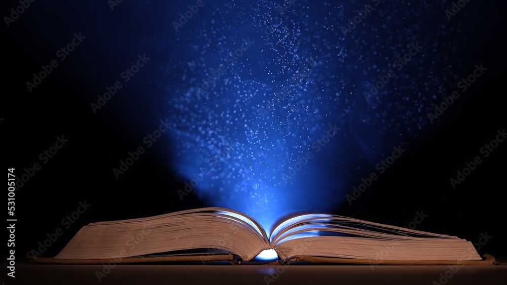 An open book illuminated by beam of blue light with smoke and dust