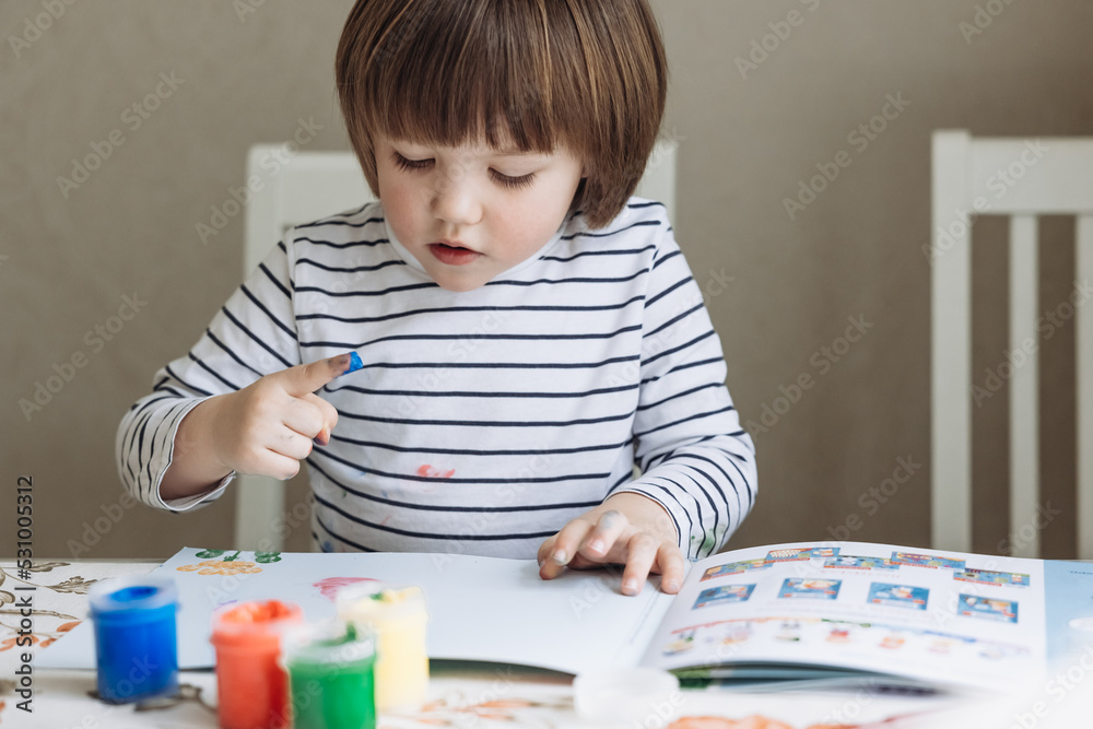Finger painting. Portrait of cute little boy painting with fingers at home. Close-up of child's hand in colorful paints. Early education concept. Sensory play. Development of fine motor skills. Finger painting. Portrait of cute little boy painting with fingers at home. Close-up of child's hand in colorful paints. Early education concept. Sensory play. Development of fine motor skills.