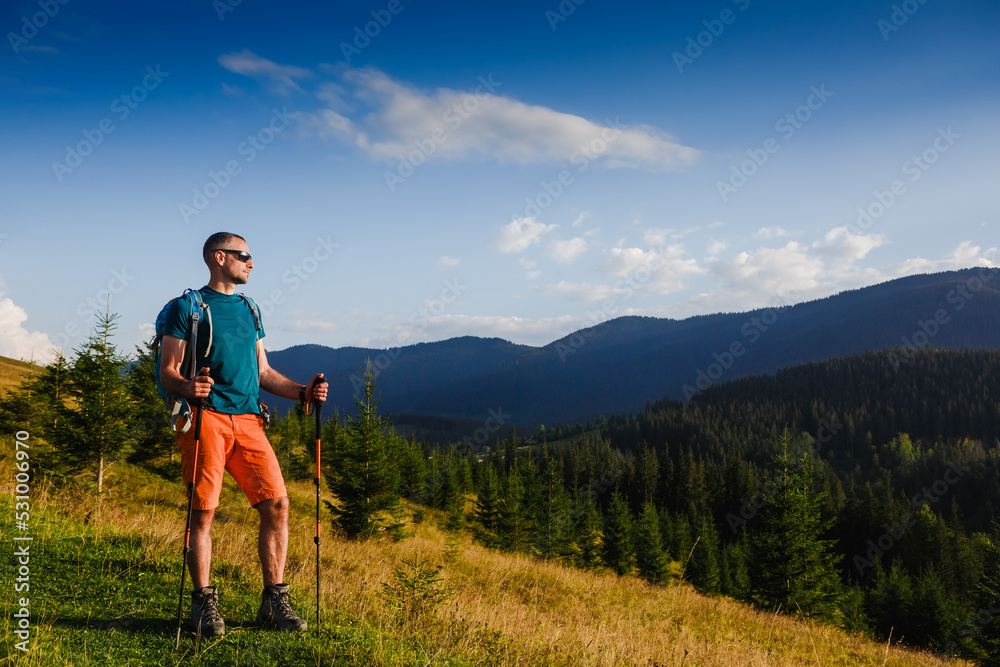 Hiker walking in mountains with poles on path in mountains at sunset. Lifestyle success concept adventure active vacations outdoor mountaineering sport
