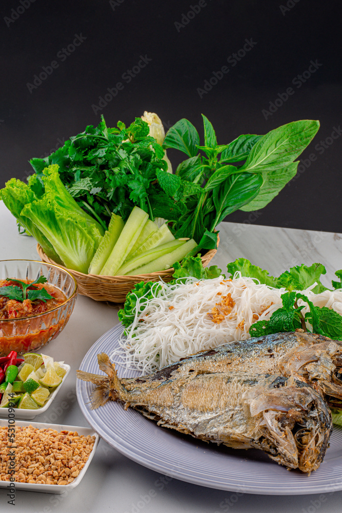 Fried two short bodied mackerel fishes and vegetable on white plate on black table Fried two short bodied mackerel fishes and vegetable on white plate on black table