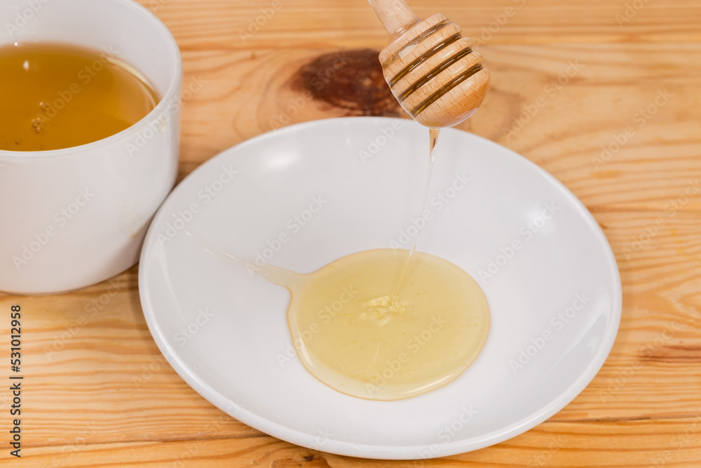 Honey flowing from the wooden honey dipper on to saucer Honey flowing from the wooden honey dipper on to saucer
