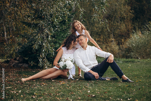 Family mother, father and daughter are beautiful and happy together on a holiday, in white clothes and with a bouquet, in nature