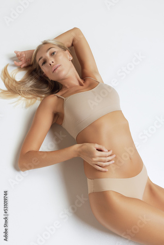 Aerial view of sportive young woman in underwear lying on floor on grey background. Fitness, diet, skin and body care.