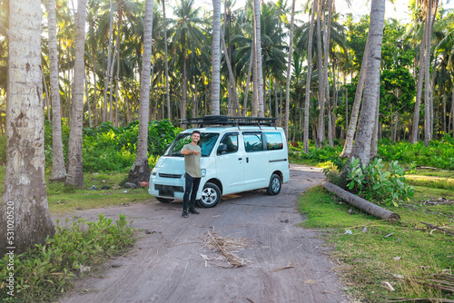 young man in front of white camper van parked in tropical scenic field of Bali Indonesia at sunset © Alexander White