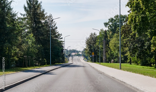 Asfaltowa droga idąca przez most nad rzeką Odrą otoczona barierkami wokół oświetlenie uliczne oraz nieliczne drzewa a na tle błękitne lekko zachmurzone niebo w zachodniej Polsce