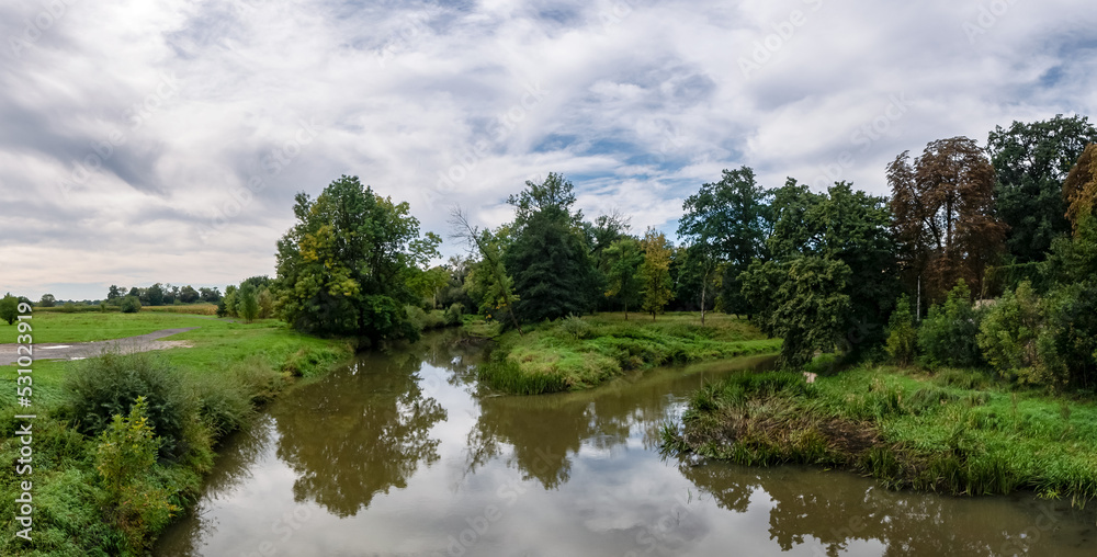 Fototapeta premium krajobraz rzeki Osobłogi w zachodniej Polsce w jasnych zielono niebieskich barwach i lekko pochmurnej pogodzie