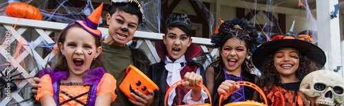 Fotografie, Obraz Multiethnic kids holding buckets while celebrating halloween outdoors, banner