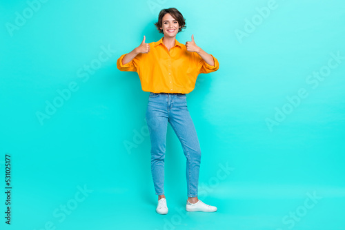 Full length photo of cheerful pretty lady stand empty space arm demonstrate yes quality symbol isolated on cyan color background