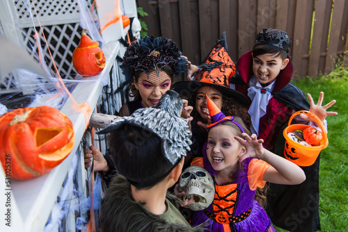High angle view of multiethnic kids frightening friend during halloween celebration in backyard