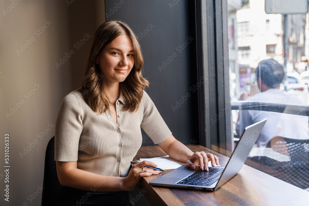 Shot of glad female businessperson with laptop waiting for coffee in coffee bar. Shot of glad female businessperson with laptop waiting for coffee in coffee bar.