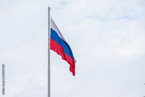 The state symbol of the Russian Federation in the wind. A large Russian flag against a blue sky with clouds in close-up.