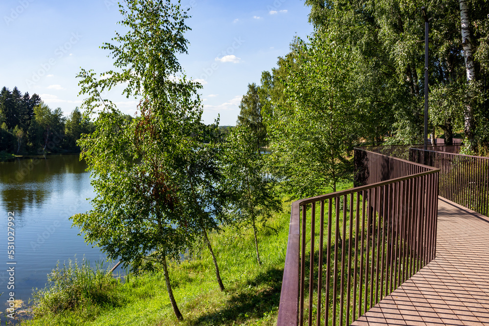 A beautiful promenade overlooking the lake, wooden walkways with railings. Pond on Stradalovka in Balabanovo, Russia A beautiful promenade overlooking the lake, wooden walkways with railings. Pond on Stradalovka in Balabanovo, Russia