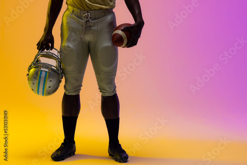 Midsection of african american male american football player with neon purple and yellow lighting