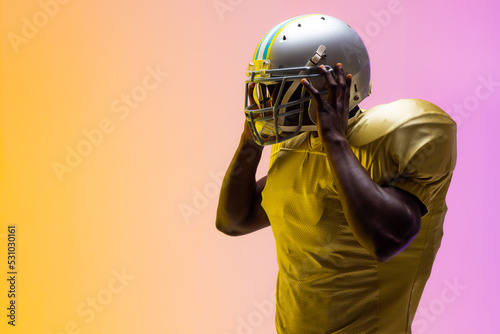 African american male american football player wearing helmet with neon yellow and purple lighting © wavebreak3