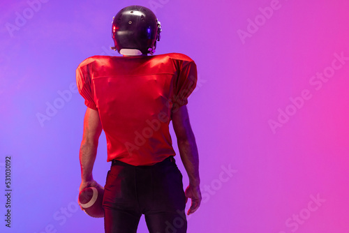 Fototapeta Naklejka Na Ścianę i Meble -  Caucasian male american football player holding ball with neon blue and purple lighting
