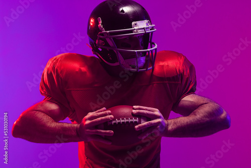 Caucasian male american football player holding ball with neon blue and purple lighting