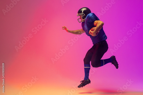 Caucasian male american football player holding ball with neon pink lighting