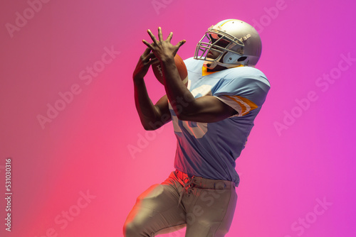 African american male american football player holding ball with neon pink lighting