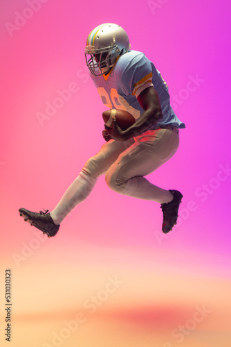African american male american football player holding ball with neon pink lighting