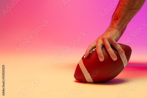Hand of caucasian male american football player holding ball with neon pink lighting
