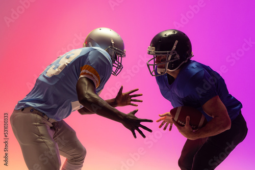 Diverse male american football players holding ball with neon pink lighting