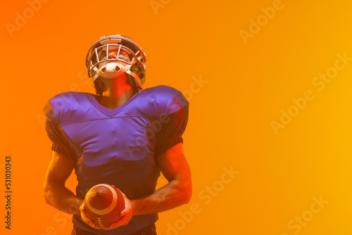 Caucasian male american football player holding ball with neon orange lighting