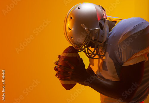 African american male american football player holding ball with neon orange lighting