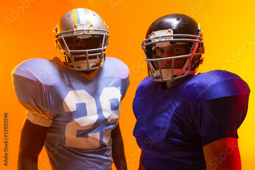 Diverse male american football players wearing helmets with neon orange lighting