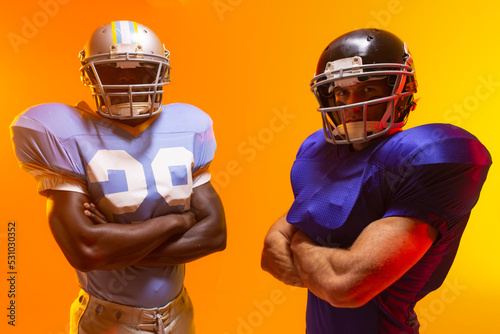 Diverse male american football players wearing helmets with neon orange lighting