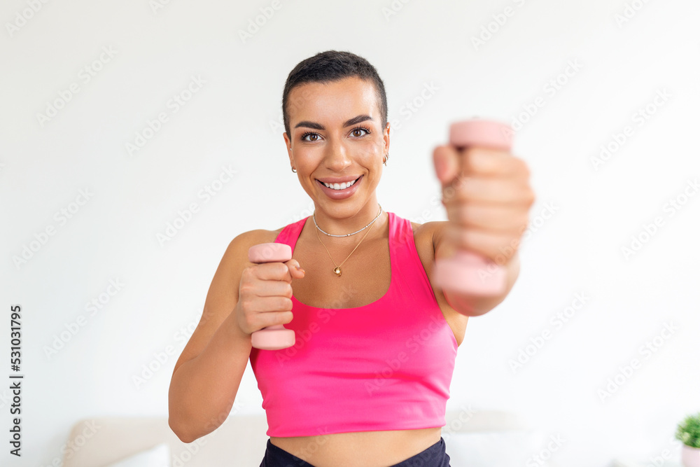 Domestic Training With Weights. Positive black lady doing exercises with dumbbells, strengthening her body at home. Smiling young female working on her biceps muscles, staying healthy Domestic Training With Weights. Positive black lady doing exercises with dumbbells, strengthening her body at home. Smiling young female working on her biceps muscles, staying healthy