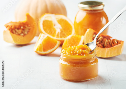 Φωτογραφία Spoon of tasty pumpkin jam on jar, slices of orange and pumpkin on light background