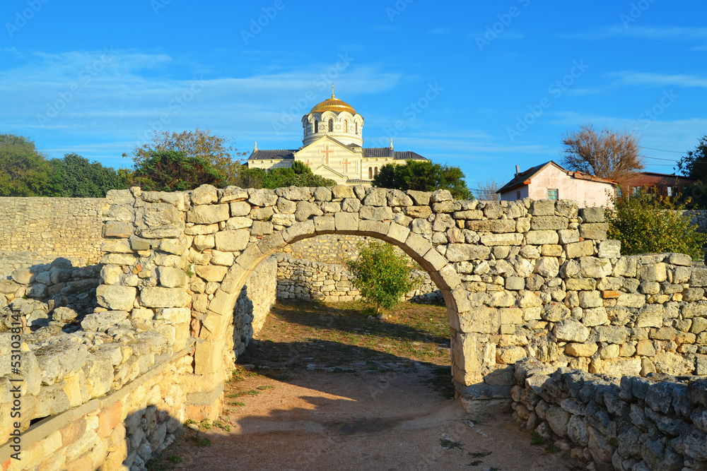 Ancient stone wall and arch in Chersonesos with a view of St. Vladimir's Cathedral under the blue sky